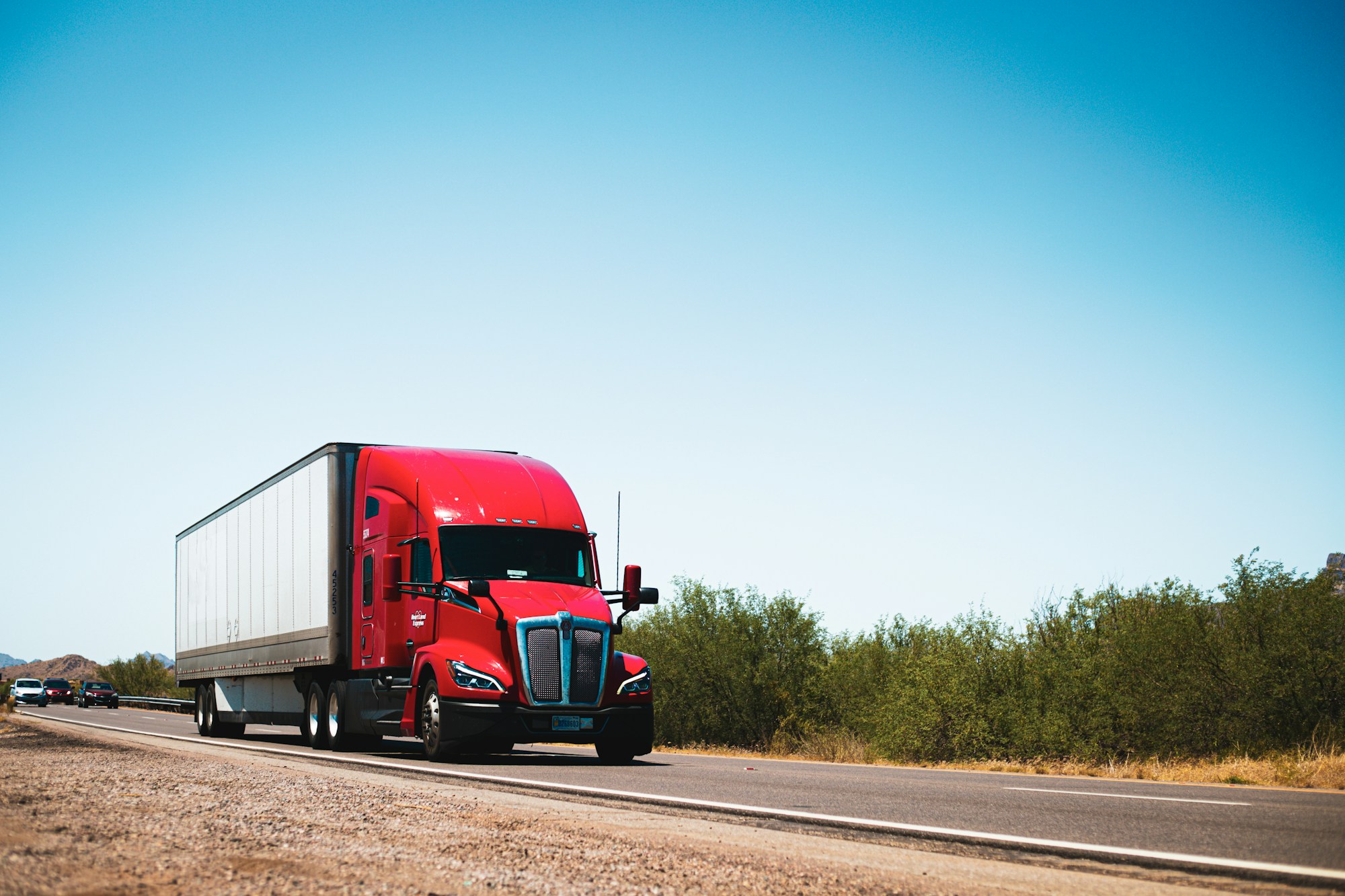 Red semi truck transporting freight along a rural highway